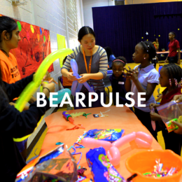 Mercer students stand at table with elementary students making balloon animals. Image is a button that links to page about BearPulse.