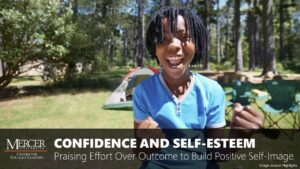 An elementary-aged boy wearing a blue shirt stands in a clearing in the woods. There is a tent and two camp chairs behind him. He smiles with an open mouth and his arms are bent at the elbows with fists clenched in a celebratory gesture. The image is a thumbnail for the module entitled Confidence and Self-Esteem: Praising Effort Over Outcome to Build Positive Self-Image.