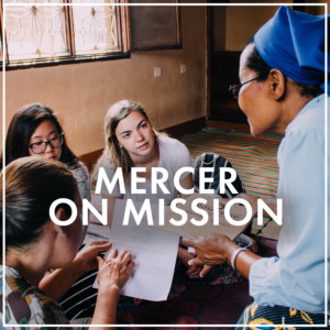 Three college students sit on the floor listening to an older woman, who sits in a chair and holds a booklet. Image is a button link to the Mercer On Mission subpage.