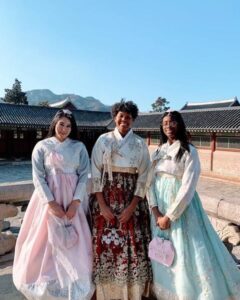 Three college women wearing South Korean traditional women's dresses stand in front of a building.