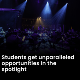 Mercer students playing string instruments on stage under blue lights.